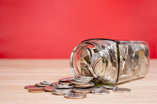 Coins spilling from a money jar on table with red background.
