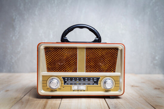 Retro old fashioned radio receiver on wooden table with concrete wall background.