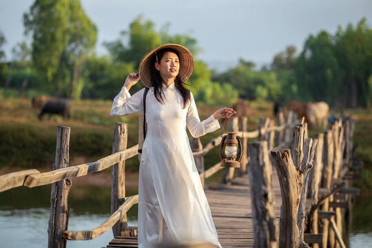 Beautiful Vietnamese girl in traditional dress holding a lantern standing on a wooden bridge in the countryside