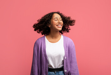 Portrait of smiling African American female model posing with healthy curly flying hair on pink...