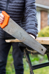Close up of an unknown person using a hand saw to cut up a plank of wood. DIY, construction, home improvement concept