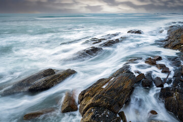 Obraz premium waves and rocks under cloudy sky in long exposure