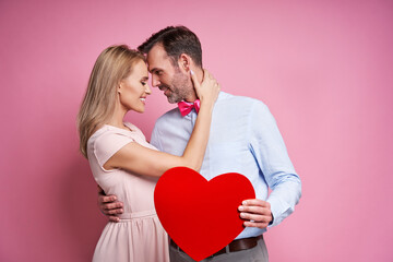 Fototapeta na wymiar Studio shot of caucasian couple on pink background bonding and holding a big red heart