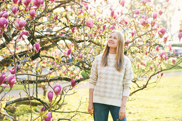 Outdoor portrait of beautiful happy model with blond hair posing next to magnolia flowers