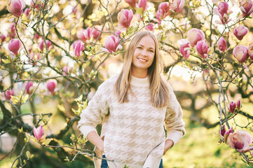 Outdoor portrait of beautiful happy model with blond hair posing next to magnolia flowers