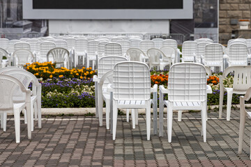 Open air cinema with group of white plastic chairs and black screen in summer day without people