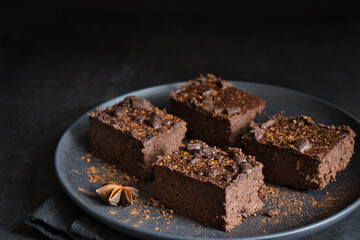 Horizontal studio shot of delicious home-made brownie cakes with pieces of dark chocolate on a plate. Dark moody food photography style with selective focus and copy space