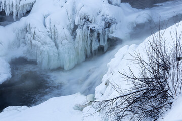 Detail of the snowy banks of the St. Charles River with the Kabir Kouba Waterfall and icicles in...