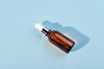 A glass bottle with a pipette with oil, serum brown on a blue background. Flat Lay