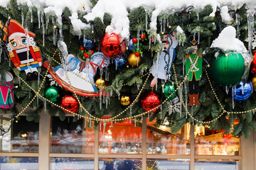 Street garland of fir branches, balls and toys, sprinkled with snow, on a wooden wall. Place for...