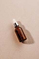 Skincare with beauty cosmetic face serum. Glass brown bottle with a pipette on a textured background with sand. Essential oil for moisturizing body skin. Copy space