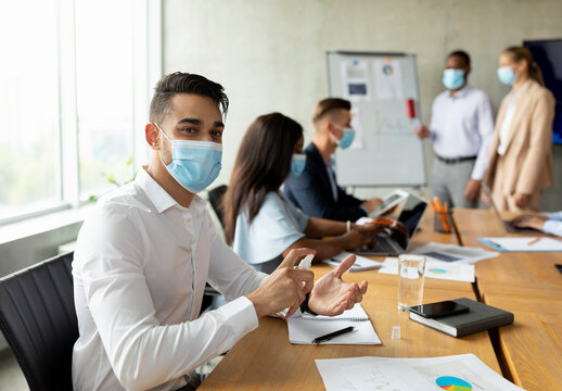 Workplace Safety. Arab Businessman Wearing Medical Mask Using Disinfectant Spray In Office