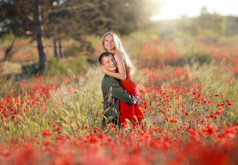 a beautiful young guy and a girl in a red dress hug and have fun in a field with poppies.