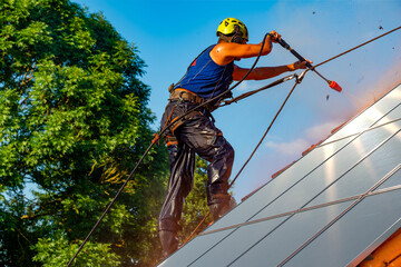 Worker washing photovoltaic panels on roof with pressurized water