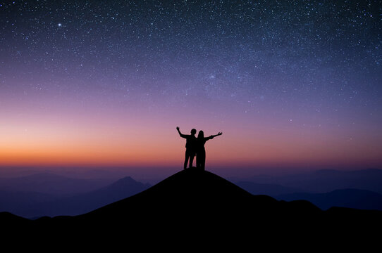 Silhouette of young couple standing with both hands above your head watched the star and milky way on top of the mountain. Couple enjoyed traveling and was successful when he reached the summit.