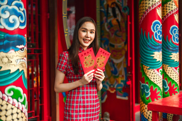 Obraz na płótnie Canvas Beautiful Asian woman wearing a traditional red cheongsam on Chinese New Year.Hand holding red envelope or Ang pao with Chinese character means happiness or good fortune.