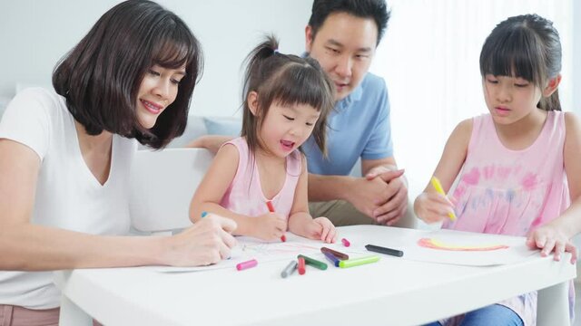 Asian young kid daughter coloring and painting on paper with parents.