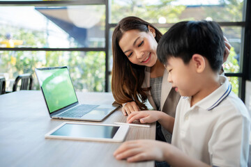 Businesswoman sitting beside kid and teach homework in the coffee shop. Woman stroking child's head and smile with copy space. Boy feeling happy during learning. Education and weekend concept.