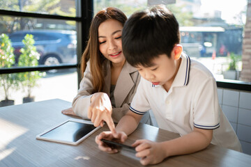 Woman point to the phone and talk with child. A boy playing game on the smartphone and sitting with his sister in the coffee shop or cafe.  Learning from internet. Education and relaxation concept.