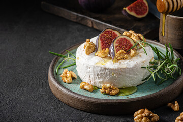 Brie or camembert cheese with figs, walnuts, honey and rosemary on dark background. Low key