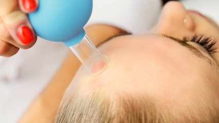 Beautician cosmetologist makes face vacuum massage with cupping cup, professional cosmetic...