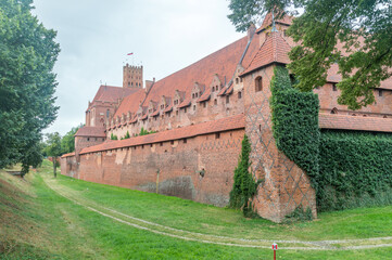 Moat with defence wall of Malbork castle at cloudy day. - obrazy, fototapety, plakaty