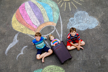 Happy little toddler girl and two kid boys flying in hot air balloon painted with colorful chalks...
