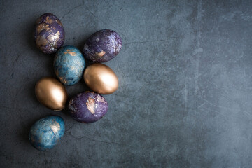 Easter card with a copy of the place for the text. Purple, blue and golden eggs on a dark background. The purple hue trend of 2022 is very relevant. Natural dye karkade tea. Top view.
