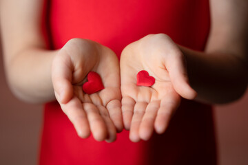 Palms of hands of obscured little girl in red clothes holding little red hearts