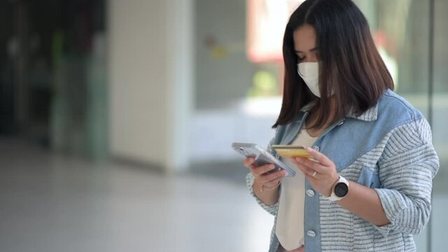 Woman wearing protection face mask prevent Coronavirus Disease (Covid-19) using credit card and mobile phone for online shopping , credit card mockup