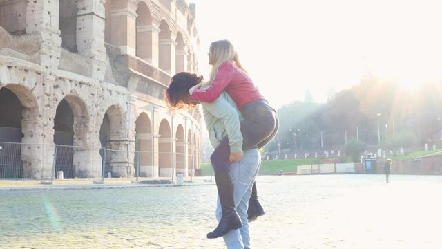 Young couple traveling to Rome. The beautiful couple is having fun in front of the Colosseum. The man picks up his girlfriend.