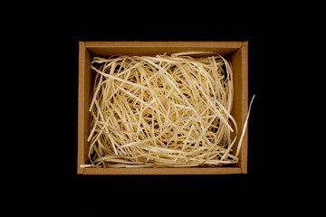 Open cardboard box for gifts from wood shavings inside on a black background. Top view.