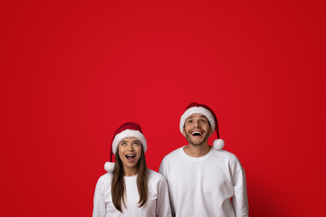 Fototapeta premium Amazing Offer. Excited Young Couple In Santa Hats Looking Up With Amazement