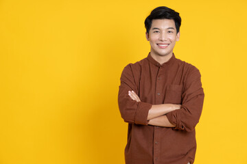 Smiling young Asian man with arms crossed in yellow studio isolated background
