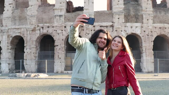 Young couple traveling to Rome. The beautiful couple is taking funny selfies in front of the Colosseum.
