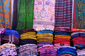 Artistic variety shade tone colors ornaments patterns, closeup view of stacked saris or sarees in display of retail shop.