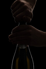 Hands opening Champagne bottle in studio setting on black background