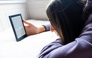 Young Adolescent GIrl is focused reading an electronic romance with her Ebook Reader while she is...