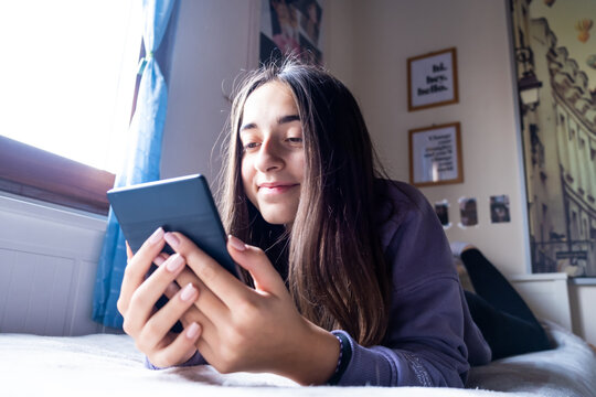 Young Teenager GIrl is focused reading an electronic book with her Ebook Reader while she is on the bed.