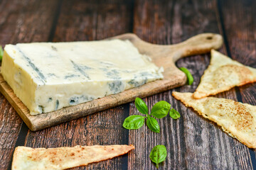 Gorgonzola cheese on cutting board with fresh  basil  and  home made crispy nachos  with spicy red sauce. Veined Italian  blue cheese. 