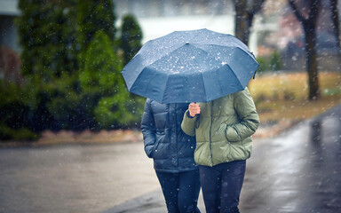 Two mid aged women walking under umbrella during snowfall in city street, Selective focus. Female...
