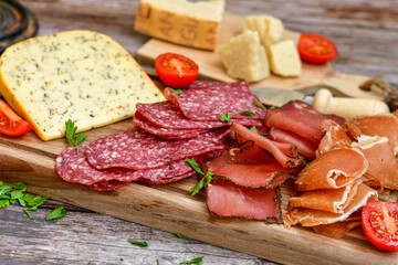 Italian  dried thinly sliced   artisan  pork Salami Milano ,  mediterranean Parmesan cheese, tomatoes   and fresh basil on wooden background .Rustic  home made Italian snack.