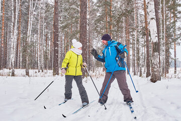 Quarrel of mature couple in winter sportswear are cross-country skiing in snowy forest.