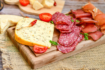 Italian  dried thinly sliced   artisan  pork salami Milano ,  mediterranean parmesan cheese, tomatoes   and fresh basil on wooden background .Rustic  home made italian snack.