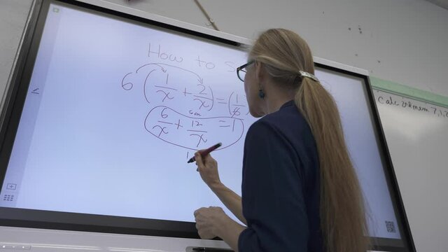 Low angle view of female teacher writing on an interactive whiteboard teaching math in a classroom.
