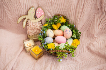 On a pastel bedspread is a basket of grass and various bright flowers, a rabbit. The basket contains Easter eggs painted with watercolors in beautiful pastel colors.