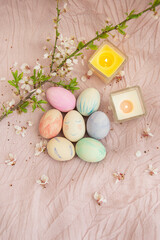 Beautiful watercolor paints on Easter eggs that lie on a delicate pink cloth along with burning candles. Easter concept.