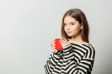 Beautiful girl in striped sweater with red mug on white background