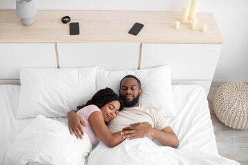 Calm millennial african american female and male sleeping at night, hugging on bed in bedroom interior
