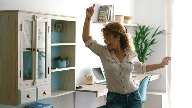Excited and joyful middle age woman dancing at home singing a song for happiness - single people lifestyle and joy emotions concept - beautiful mature female happy in living room healthy lifestyle